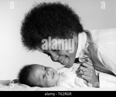 1970s SMILING AFRICAN AMERICAN MOTHER HOLDING HAND AND LOOKING AT HAPPY BABY DAUGHTER LYING ON HER BACK - b24811 HAR001 HARS OLD FASHION 1 JUVENILE FACIAL YOUNG ADULT INFANT STRONG PLEASED JOY LIFESTYLE FEMALES HEALTHINESS HOME LIFE DAUGHTERS PERSONS INSPIRATION CARING SERENITY CONFIDENCE EXPRESSIONS B&W HAPPINESS HEAD AND SHOULDERS CHEERFUL STRENGTH AFRICAN-AMERICANS AFRICAN-AMERICAN AND BLACK ETHNICITY PRIDE AT ON SMILES JOYFUL STYLISH PERSONAL ATTACHMENT AFFECTION EMOTION GROWTH JUVENILES MOMS TOGETHERNESS YOUNG ADULT WOMAN AFRO HAIR STYLE BABY GIRL BLACK AND WHITE HAR001 OLD FASHIONED Stock Photo