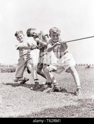 1930s 4 BOYS PULLING ON ROPE PLAYING TUG OF WAR ON PLAYGROUND ALL