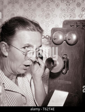 1930s 1940s ELDERLY MATURE WOMAN LOOKING AT CAMERA SPEAKING GOSSIPING ON OLD FASHIONED WOODEN CRANK WALL TELEPHONE - bt00141 CAM001 HARS COMMUNICATING COPY SPACE LADIES PERSONS CONFIDENCE EYEGLASSES GOSSIPING SENIOR ADULT MIDDLE-AGED B&W EYE CONTACT SENIOR WOMAN MIDDLE-AGED WOMAN OLDSTERS HEAD AND SHOULDERS OLDSTER EXCITEMENT PROGRESS RECREATION CAM001 PHONES ELDERS CONNECTION TELEPHONES BLACK AND WHITE CAUCASIAN ETHNICITY OLD FASHIONED OLD-FASHIONED SUSPICIOUS WALL PHONE Stock Photo