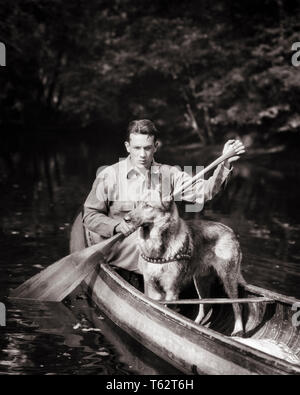 1920s YOUNG OUTDOORSMAN PADDLING CANOE ON WOODLAND STREAM WITH GERMAN SHEPHERD DOG AS PASSENGER  - c2064 HAR001 HARS MAMMALS ADVENTURE DISCOVERY LEISURE STRENGTH CANINES RECREATION AS ON MASTER POOCH CONCEPTUAL OUTDOORSMAN SPORTSMAN CANINE GERMAN SHEPHERD MAMMAL PADDLING RELAXATION TOGETHERNESS WOODLAND YOUNG ADULT MAN BLACK AND WHITE CAUCASIAN ETHNICITY HAR001 OLD FASHIONED Stock Photo