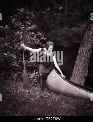 1910s 1920s SERIOUS YOUNG WOMAN IN SPORTSWOMAN BATHING SUIT HOLDING PADDLE PULLING CANOE ON TO BANK OF STREAM - c24 HAR001 HARS COPY SPACE FULL-LENGTH LADIES PERSONS STREAM ATHLETIC CONFIDENCE TRANSPORTATION EXPRESSIONS B&W ACTIVITY PADDLE PHYSICAL ADVENTURE LEISURE STRENGTH RECREATION IN OF ON TO CONCEPTUAL ATHLETES FLEXIBILITY MUSCLES STYLISH BATHING SUIT SPORTSWOMAN RELAXATION YOUNG ADULT WOMAN BLACK AND WHITE CAUCASIAN ETHNICITY HAR001 OLD FASHIONED Stock Photo