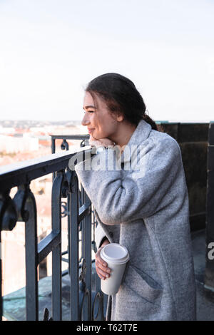 Girl stands on balcony with cup of coffee in hand Stock Photo