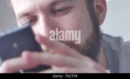 A young bearded man uses his mobile phone. Close-up shot, focus on eyes. Stock Photo