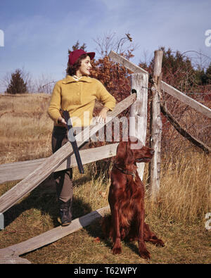 1950s WOMAN UPLAND BIRD HUNTER RED CAP YELLOW SWEATER LEANING ON WOOD FENCE HOLDING SHOTGUN COUNTRY LIFESTYLE  IRISH SETTER DOG - kg3247 LAW001 HARS RELAXING IRISH LIFESTYLE FEMALES RURAL GROWNUP HEALTHINESS COPY SPACE FULL-LENGTH LADIES PERSONS GROWN-UP HUNTER CONFIDENCE HUNT TIME OFF PEOPLE STORY SKILL ACTIVITY AMUSEMENT STRUCTURE HAPPINESS MAMMALS ADVENTURE HOBBY TRIP INTEREST GETAWAY CANINES HOBBIES KNOWLEDGE LOW ANGLE RECREATION PASTIME SETTER PLEASURE ON HOLIDAYS POOCH SPLIT RAIL IRISH SETTER STYLISH LEANS UPLAND CANINE FIREARM FIREARMS GUNNING MAMMAL MID-ADULT MID-ADULT WOMAN RELAXATION Stock Photo