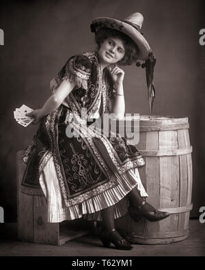 1890s 1900s SMILING WOMAN HIDING POKER CARDS BEHIND HER BACK WEARING MEXICAN STYLE COSTUME LEANING ON WOODEN BARREL - o2779 HAR001 HARS FEMALES HIDING STUDIO SHOT COPY SPACE HALF-LENGTH LADIES PERSONS CHARACTER RISK WESTERN ENTERTAINMENT BARREL MEXICAN B&W GAMBLING POKER CHEERFUL STYLES SOMBRERO CHARACTERS SALOON ACTRESS ENTERTAINER SMILES CARD GAME STYLISH DANCE HALL FASHIONS YOUNG ADULT WOMAN BLACK AND WHITE CAUCASIAN ETHNICITY GAMBLER HAR001 OLD FASHIONED Stock Photo