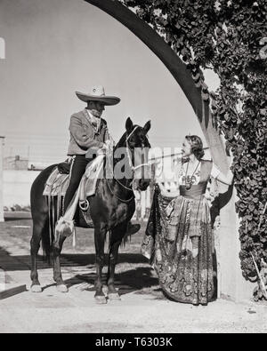 1930s SMILING CAUCASIAN WOMAN IN TRADITIONAL CHINA POBLANA COSTUME TALKING TO MEXICAN MAN HORSEACK WEARING CHARRO COWBOY CLOTHES - r11452 HAR001 HARS LIFESTYLE HISTORY FEMALES RURAL COPY SPACE FRIENDSHIP FULL-LENGTH LADIES PERSONS TRADITIONAL MALES TRANSPORTATION MEXICAN B&W NORTH AMERICA MEXICO ADVENTURE STYLES LATIN AMERICAN STYLISH FASHIONS MID-ADULT MID-ADULT MAN YOUNG ADULT WOMAN BLACK AND WHITE CAUCASIAN ETHNICITY CHARRO CHINA POBLANA HAR001 HISPANIC ETHNICITY OLD FASHIONED TOURISM Stock Photo