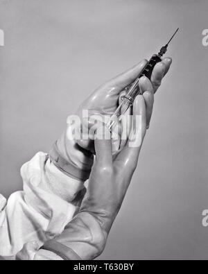 1940s HANDS WEARING RUBBER GLOVES PREPARING TO ADMINISTER INJECTION BY HYPODERMIC NEEDLE - s10474 HAR001 HARS HEALING PHYSICIANS HEALTH CARE BY TO AUTHORITY MEDICATION OCCUPATIONS CONCEPT HEALER CONCEPTUAL PHYSICIAN PRACTITIONER HYPODERMIC RUBBER GLOVES SYMBOLIC ADMINISTER CONCEPTS PROFESSIONALS BLACK AND WHITE HANDS ONLY HAR001 OLD FASHIONED REPRESENTATION Stock Photo