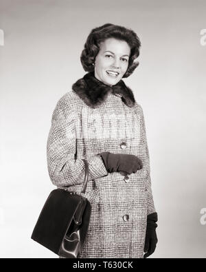 1960s BRUNETTE WOMAN WEARING GLEN PLAID WOOL COAT WITH FUR COLLAR CARRYING POCKETBOOK STANDING OUTDOOR TALKING LOOKING AT CAMERA - s11593 HAR001 HARS COMMUNICATION PLEASED JOY LIFESTYLE SATISFACTION FEMALES WOOL COPY SPACE HALF-LENGTH LADIES PERSONS PLAID CONFIDENCE EXPRESSIONS B&W EYE CONTACT BRUNETTE SUCCESS HOMEMAKER HOMEMAKERS CHEERFUL LEISURE STRENGTH STYLES CHOICE LEADERSHIP PRIDE HOUSEWIVES SMILES FUR COLLAR CONCEPTUAL JOYFUL STYLISH POCKETBOOK FASHIONS MID-ADULT MID-ADULT WOMAN BLACK AND WHITE CAUCASIAN ETHNICITY HAR001 OLD FASHIONED Stock Photo