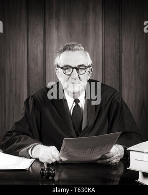 1940s 1950s SERIOUS MAN JUDGE SEATED WEARING ROBE WITH GAVEL AT HAND HOLDING PAPERS  LOOKING AT CAMERA - s7404 HAR001 HARS COMMUNICATION GAVEL LIFESTYLE ELDER JOBS ROBE COPY SPACE HALF-LENGTH PERSONS MALES CONFIDENCE SENIOR MAN SENIOR ADULT EXPRESSIONS MIDDLE-AGED B&W MIDDLE-AGED MAN EYE CONTACT FREEDOM SKILL SUIT AND TIE OCCUPATION SKILLS OLDSTERS OLDSTER ROBES JUDICIAL LAWYERS LEADERSHIP POWERFUL STERN JUDGMENT ATTORNEYS AUTHORITY OCCUPATIONS POLITICS ELDERS CONCEPTUAL ATTORNEY COOPERATION BLACK AND WHITE CAUCASIAN ETHNICITY DIRECT HAR001 OLD FASHIONED Stock Photo