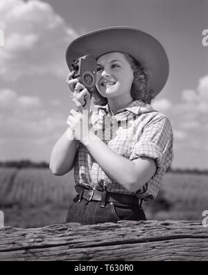 1940s SMILING YOUNG WOMAN IN COWBOY HAT AND WESTERN CLOTHES PHOTOGRAPHING USING HAND HELD 8MM HOME MOVIE CAMERA - u532 HAR001 HARS HOBBY LEISURE INTEREST AND EXCITEMENT HOBBIES KNOWLEDGE RECREATION PASTIME PHOTOGRAPHING PLEASURE IN SMILES USING CONCEPTUAL JOYFUL STYLISH 8MM HAND HELD RELAXATION YOUNG ADULT WOMAN AMATEUR BLACK AND WHITE CAUCASIAN ETHNICITY ENJOYMENT HAR001 OLD FASHIONED Stock Photo