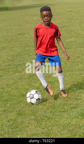 Hampshire, England, UK. April 2019. A nine year old footballer dribbles the soccer ball during a training session in a public park. Stock Photo