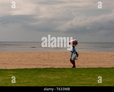 Bali, Indonesia -- February 29, 2016. An Indonesian woman carries goods in the traditional way as she walks on the beach. Stock Photo