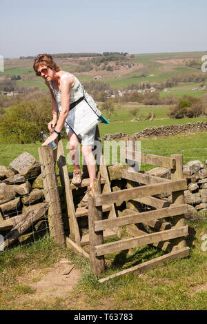 Woman climbing over a stile in a dry stone wall while walking in Nidderdale in the Yorkshire Dales England UK Stock Photo