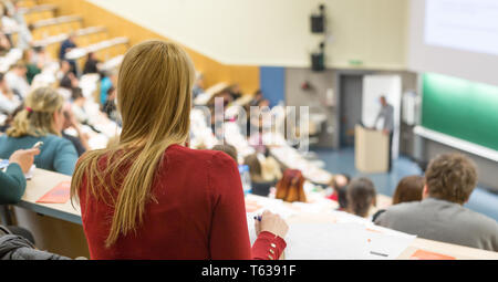 Audience in the lecture hall. Female student making notes. Stock Photo