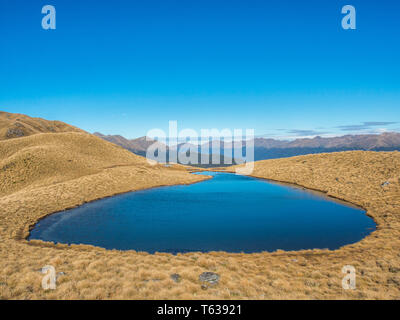 Alpine tarn,  in tussock country, above the treeline, view of distant mountains, Mt Burns Track, Fiordland National Park, Southland, New Zealand Stock Photo