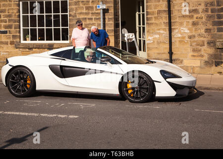 McLaren sports car being driven by elderly man and admired by two people standing at the roadside Stock Photo