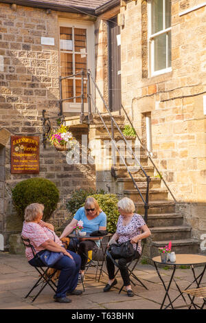 Three women sitting at cafe table outside in sunshine in the town of Pateley Bridge in the Yorkshire Dales England Stock Photo