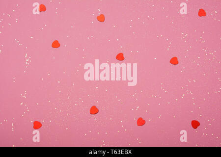 Golden glitter and hearts scattered on the pink card background, top view, selective focus Stock Photo