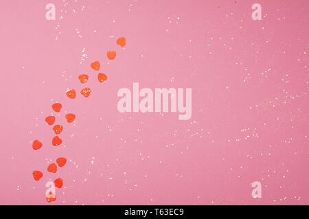 Golden glitter and hearts scattered on the pink card background, top view, selective focus Stock Photo