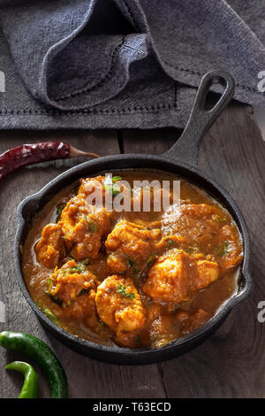 Close up traditional Indian butter chicken curry and lemon served with chapati bread in iron-cast. Wooden background.