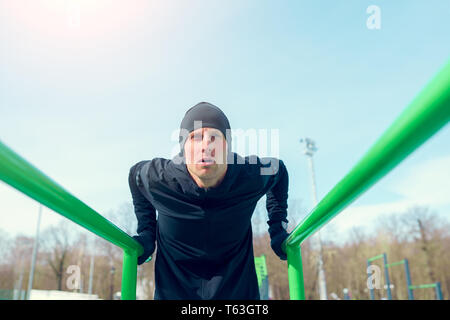 Photo of young athlete man pulling up on green horizontal bar Stock Photo