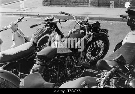 A black and white photograph taken in the 1970s showing details of a Brough Superior SS80 Motorcycle, and a Triumph Motorcycle, both classic British motorbikes. A moped can also be seen. Stock Photo