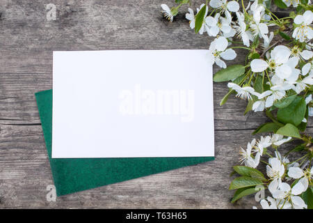 white cherry flowers on old wooden boards, cherry branch. A sheet of white paper for your text. View from above. Stock Photo