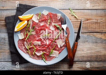 Marbled beef carpaccio with arugula, lemon and parmesan cheese on wooden table. . Top view, flat lay with copy space. Stock Photo