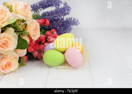Easter painted eggs with a nest and flowers of roses on a white wooden  background for the holiday Stock Photo