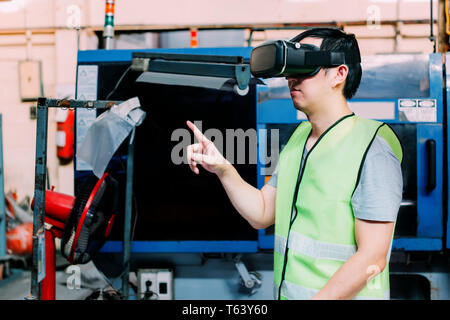 Industrial factory and manfacturing engieering worker wearing VR goggle headset touching in virtual reality simulation alongside heavy duty machines Stock Photo