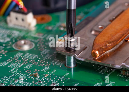 A screwdriver unscrews the mounting bolt of the computer board Disassembly, repair and cleaning of electronics. Part of laptop Stock Photo