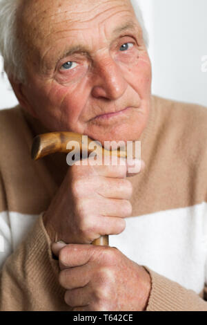 Portrait of an old sad man who put his head on the handle of a wooden cane, the concept of loneliness at home. Stock Photo
