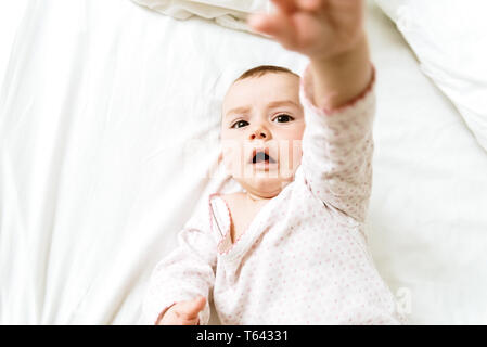 6 month old baby lying on his white bed playing with his hands. Stock Photo