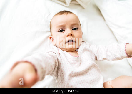 6 month old baby lying on his white bed playing with his hands. Stock Photo