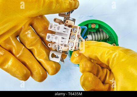 Electrician in yellow protective gloves is installing new light switch inside drywall. Stock Photo