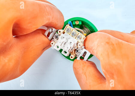 Electrician in protective gloves is installing double switch placed in the socket. Stock Photo
