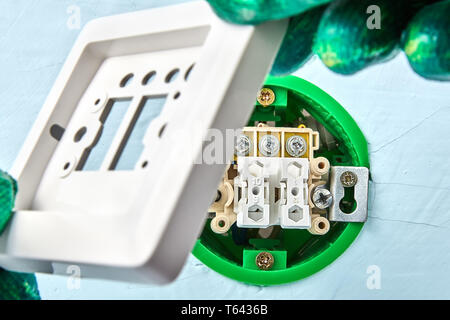 Electrician in protective gloves is putting top on new push button inside plasterboard wall, electric installation work. Stock Photo