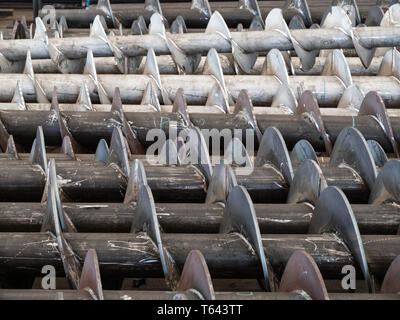 Screws for screw conveyors during production. Carbon steel screws in the foreground and stainless steel screws in the background. Stock Photo