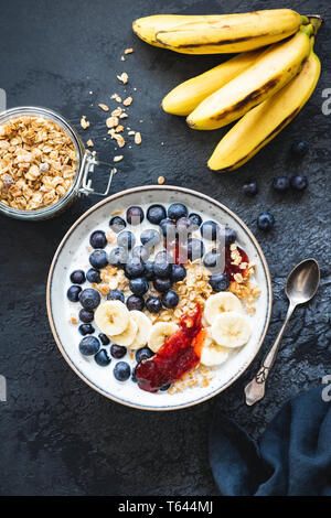 Breakfast bowl with blueberries, banana, granola and yogurt on black concrete background. Table top view. Clean eating, healthy lifestyle concept Stock Photo