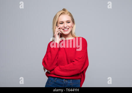 Picture of young woman dressed in red sweater talking by mobile phone isolated over grey background. Stock Photo
