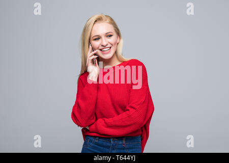 Picture of young woman dressed in red sweater talking by mobile phone isolated over grey background. Stock Photo