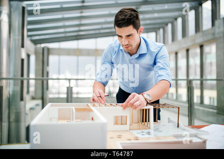 Young businessman or architect with model of a house standing at the desk in office, working. Stock Photo