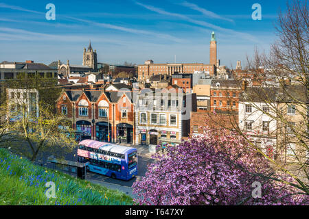 Norwich city skyline with spires of St. Peter Mancroft church and City hall tower and tourist bus passing by, viewed from Castle hill. Norfolk, UK. Stock Photo