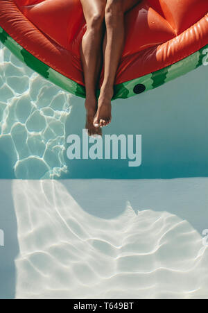 Cropped shot of woman legs on a floating mattress in swimming pool. Female sunbathing on inflatable mattress in pool. Stock Photo