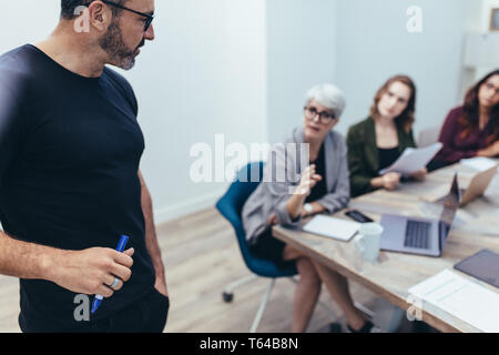 Businessman talking with colleagues during a meeting in office. Mature executive listening to suggestions from his team during a presentation. Stock Photo