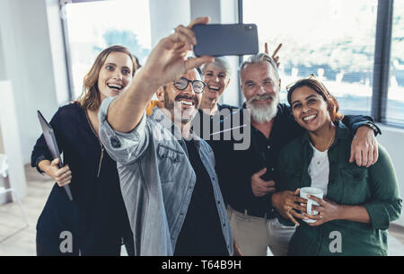 Cheerful multi-ethnic people in the office smiling and taking the selfie. businessman taking selfie with his colleagues in office. Stock Photo