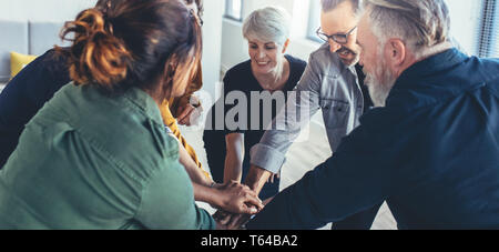 Team work and cooperation concept, people staking their hands on top of each other and smiling. Business people joining hands showing unity. Stock Photo