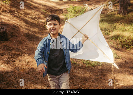 Cute boy running outdoors with a hand made kite. Child playing with a kite in forest. Stock Photo