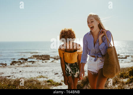 Two happy women walking along the beach. Female friends smiling while walking together at the seashore.