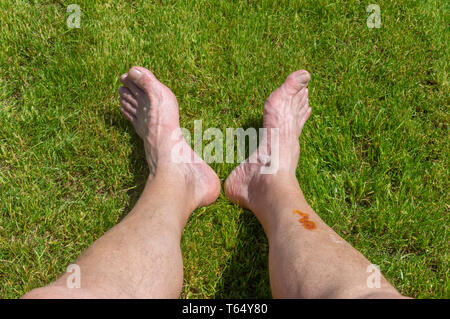Senior feet lying on a green lawn while resting after long bicycle trip Stock Photo